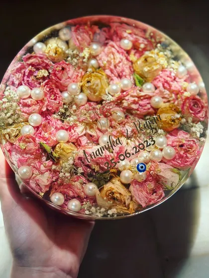 A close-up of a beautiful varmala preservation in a 7-inch circular resin piece. The pink and yellow roses are surrounded by delicate pearls, with the couple's names and date engraved.