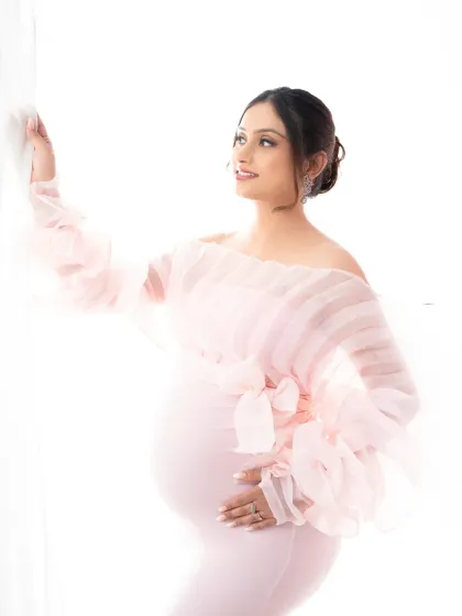 A glowing portrait by the window. The soft light illuminates the expectant mother in her pink gown, highlighting her joyful anticipation.