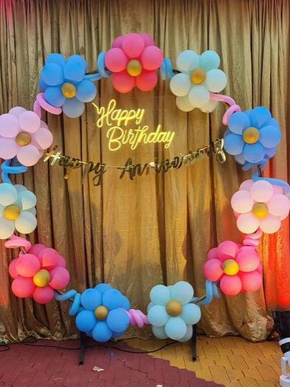 A creative and colorful birthday backdrop featuring a ring of balloon flowers in pastel shades, complete with a neon sign.