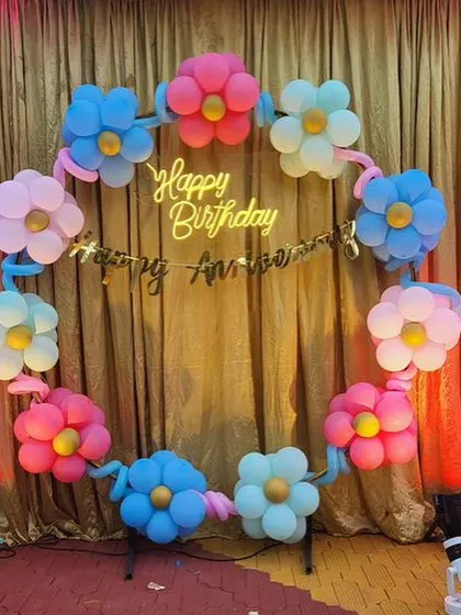 A creative and colorful birthday backdrop featuring a ring of balloon flowers in pastel shades, complete with a neon sign.