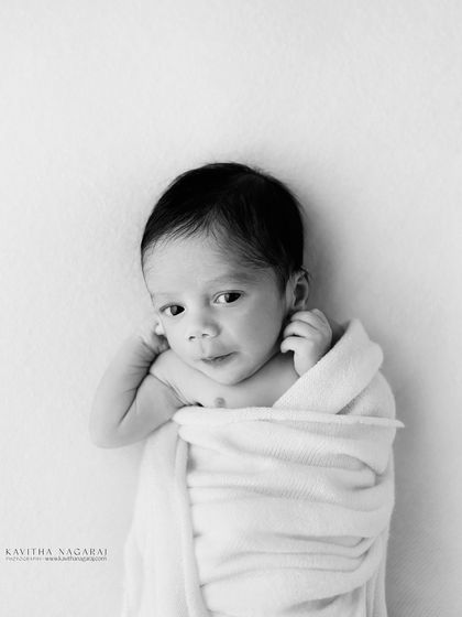 A minimalist black and white portrait of a newborn, simply wrapped. The clean, high-key look is sophisticated and timeless, focusing on the baby's innocent expression.
