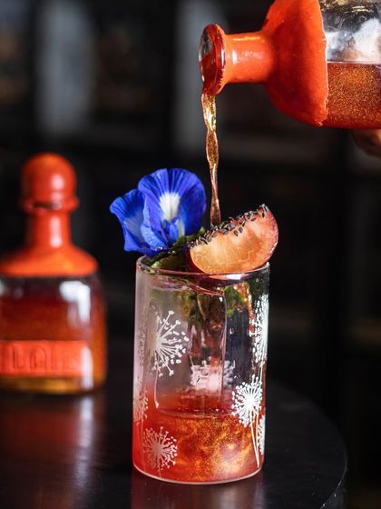 The perfect elixir for your gateway to surreal adventures. The 'Wax Bloom' cocktail being poured from its custom bottle, shimmering with edible glitter.