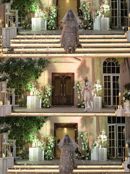 A dramatic and beautiful shot of the bride and groom's entrance. The decor features elegant white floral arrangements on stately pedestals, creating a grand and timeless setting.