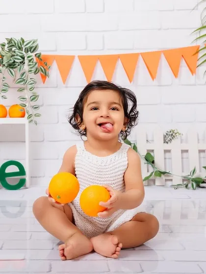 A playful moment as a one-year-old holds two oranges and sticks his tongue out for the camera.