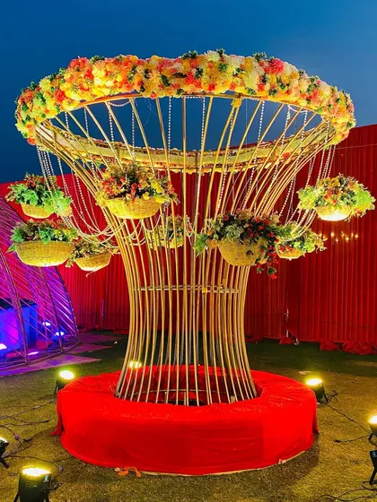 The same decorative tree at night, with spotlights highlighting its golden structure and the colorful flowers.