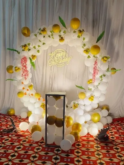 A simple and elegant birthday setup with a white and gold balloon ring. The decoration includes a "Happy Birthday" neon sign and is perfect for home celebrations.