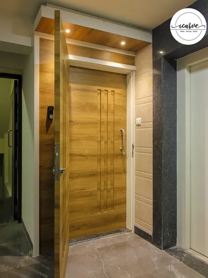 This main door design uses simple vertical grooves and a sleek handle for a modern and minimalist look. The overhead lighting highlights the wooden texture.