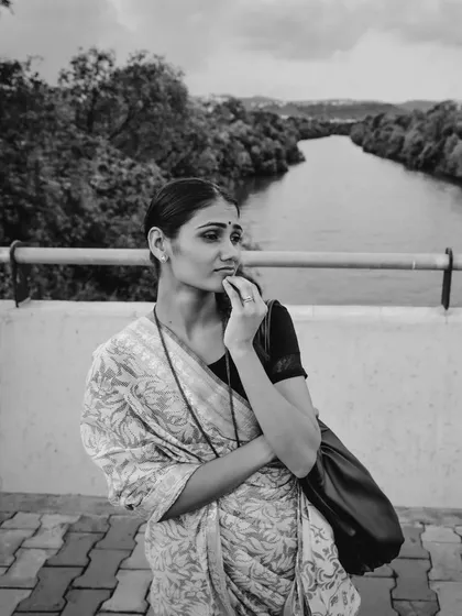 A black and white shot capturing a woman's quiet strength. Dressed in a simple saree, she looks out over the water, telling a story of resilience.