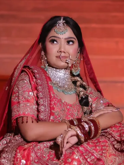 A close-up of a bride in a red lehenga, seated on grand steps with warm, dramatic lighting.