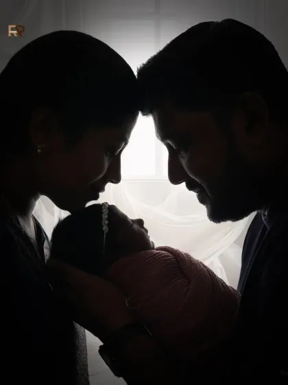 A dramatic silhouette of a new family. The parents' faces are close to their newborn's, creating an intimate and powerful image against a bright window.
