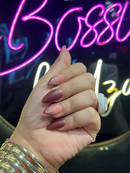 This angle highlights the sharp stiletto shape and the intricate detail of the reverse French glitter tip. The salon's neon sign in the background adds to the luxe vibe.