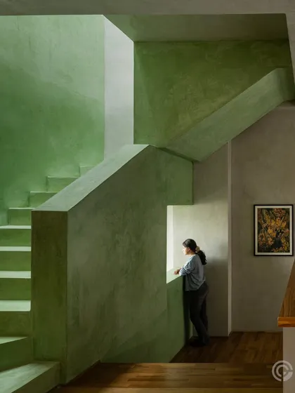 A monolithic staircase finished in a serene green oxide plaster creates a powerful play of form, light, and shadow. We use bold, continuous material applications like this to define volumes and create a tranquil, immersive experience within the home.