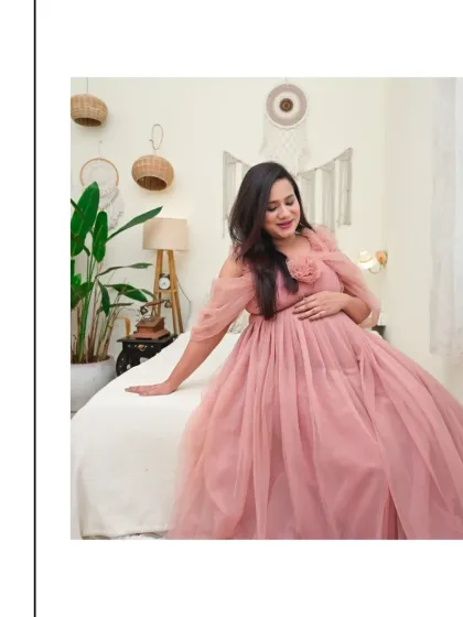 A peaceful solo portrait of a mom-to-be in a flowing pink gown. She is seated on our comfortable bed set, surrounded by the calming, natural elements of our Boho-themed studio space.