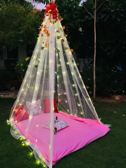 A dreamy cabana tent setup on a lawn for a unique outdoor celebration. I use a sheer canopy draped with fairy lights and floral vines to create a cozy and intimate space for you and your partner.