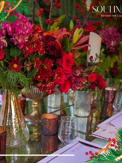 A close-up of a Christmas-themed tablescape, featuring red floral arrangements, candles, and elegant menus. Every detail is curated to create a warm and festive atmosphere.