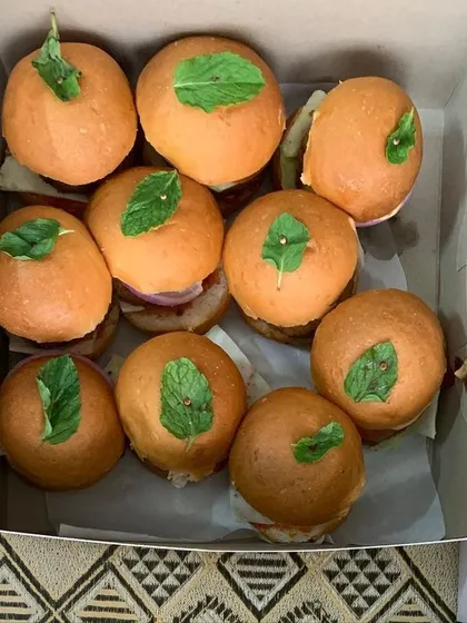 A box of mini veggie burgers with a fresh mint leaf on top.