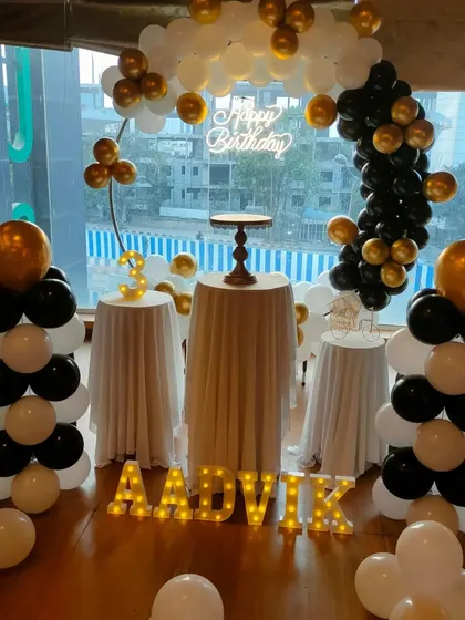 A sophisticated black, white, and gold balloon arch setup in a venue with large windows.