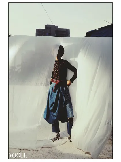 A full-body shot from a series featured in PhotoVogue, captured on 35mm film. The model, styled in Levi's, stands against a draped white sheet, creating a raw, high-contrast image that plays with shadow and form.