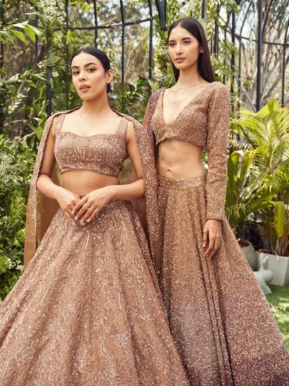 Two shimmering rose gold lehengas from the Lenora collection. With intricate handwork and flowing fabrics, this is minimalism made majestic, perfect for the modern bride or bridesmaid.