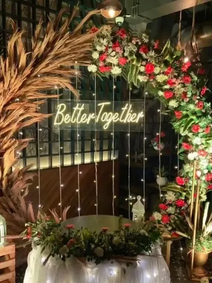 For a modern and stylish anniversary or engagement party, I designed this rustic-chic arch. It combines dried pampas grass with fresh red and white flowers, fairy lights, and a "Better Together" neon sign for a warm, inviting photo backdrop.