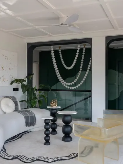 This view of the Evelyn lounge highlights the unique combination of furniture and art. The transparent resin chairs add a modern touch, while the pearl necklace chandelier provides a dramatic backdrop.