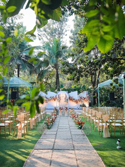 A wedding ceremony setup viewed through a frame of green leaves. The warm, earthy tones of the decor look beautiful in the morning sun.