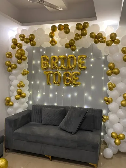 A classic and elegant 'Bride to Be' decoration for a pre-wedding celebration. The setup features a beautiful white and gold balloon arch against a backdrop of fairy lights, creating the perfect photo opportunity.
