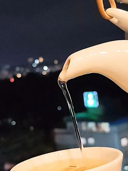 A simple, beautiful moment. Enjoy a cup of our fragrant jasmine tea being poured, with the soft, blurred lights of the Bangalore cityscape creating a serene and peaceful backdrop for your evening.