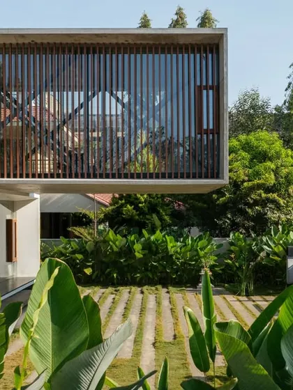 The cantilevered upper floor, with its vertical wooden louvers, creates a screened living space that is protected yet open. Below, the garden's lush foliage grows right up to the house, blurring the line between inside and out.