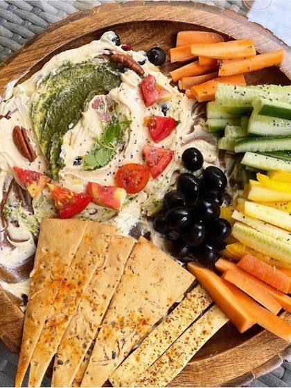A beautiful and healthy platter is perfect for sharing. This one features a creamy dip surrounded by fresh vegetable sticks like carrots and cucumbers, along with olives and low-carb crackers.