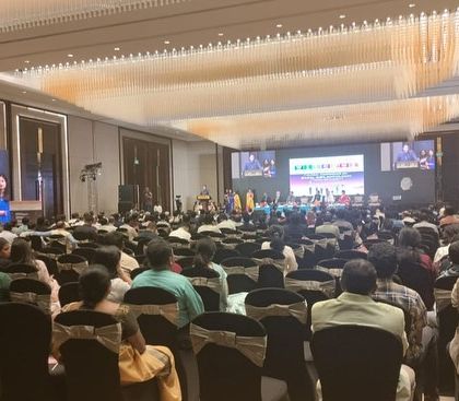 The conference is in full swing, with a packed audience and a speaker on stage. I manage the live event flow, including technical coordination for sound and visuals, to ensure a seamless presentation.