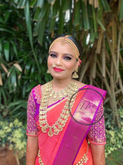 A gorgeous bride ready for her wedding. This look features bold, defined eyes with a pop of shimmer, a bright red-pink lip, and traditional gold coin jewellery (kasumalai). The matha patti frames her face beautifully, creating a classic bridal portrait.