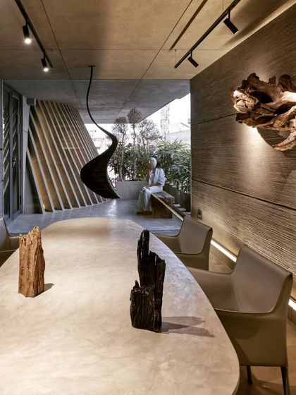 This angle highlights the interplay of light and texture in the studio. The long, concrete conference table is complemented by sculptural wood pieces and a view into the open-to-sky courtyard, creating a space that feels both grounded and expansive.