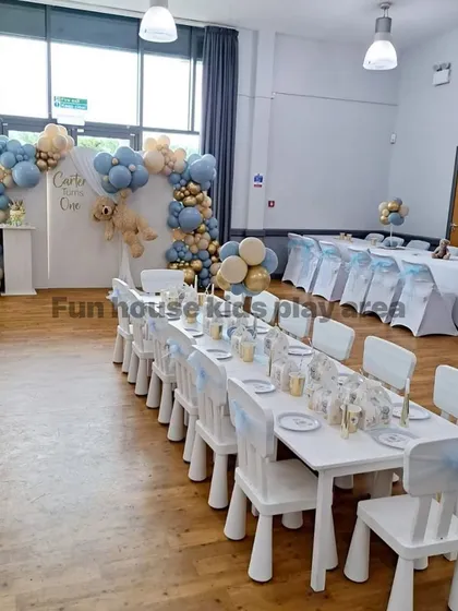 An elegant indoor setup for a first birthday party. Our white tables and chairs are beautifully arranged, complementing the sophisticated blue and gold balloon decor.