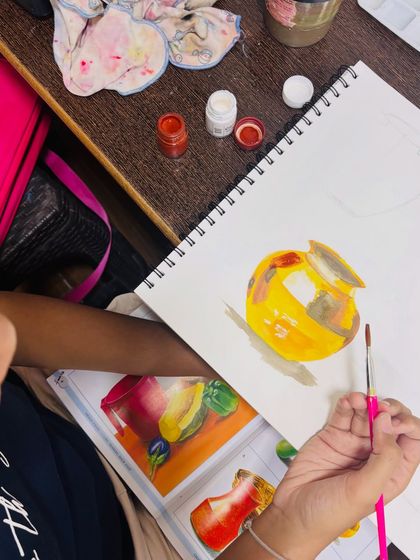 A close-up of a student's work in progress. This image shows the initial blocking of colors on the pot, which forms the base for adding detailed highlights and shadows later.