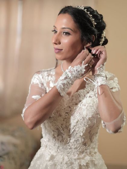 The final touches. Our bride puts on her earrings, her makeup complete. The look features cool brown tones with a silver shimmer on the eyes, perfect for her white gown.