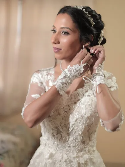 The final touches. Our bride puts on her earrings, her makeup complete. The look features cool brown tones with a silver shimmer on the eyes, perfect for her white gown.