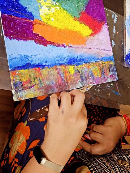 An overhead view of a student applying layers of colorful paint to her canvas during our expressive sky workshop.