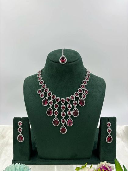 An elegant AD necklace set with a matching maang tikka. The cascading design with teardrop stones is available in green, pink, and all-white, perfect for receptions and parties.