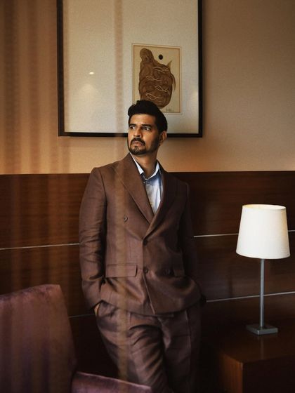 A standing portrait of Tahir Raj Bhasin. The composition uses the artwork and lamp to frame him, adding layers to the environment.