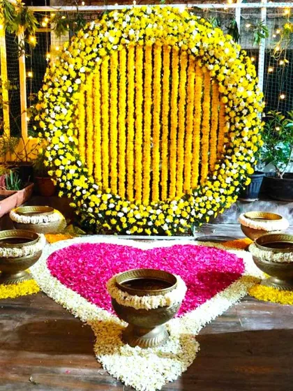 A beautiful Haldi decoration for a home terrace. The setup includes a circular marigold backdrop and a heart-shaped floral rangoli on the floor.
