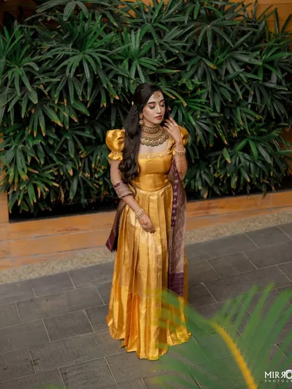 A stunning bride in a golden half-saree, perfect for a pre-wedding ceremony. The makeup is elegant with a focus on defined eyes and soft contouring.