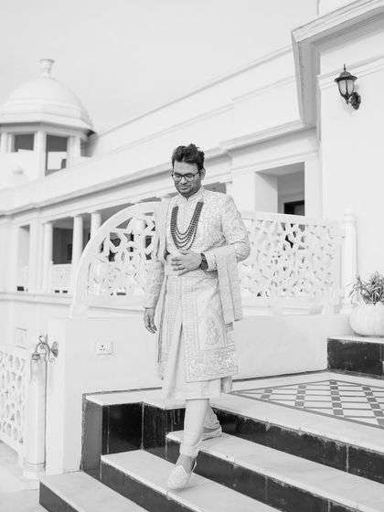 A stylish black and white portrait of the groom in his sherwani, walking down the steps of the palace.