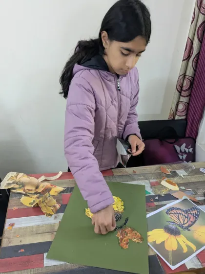 A student engaged in a collage workshop, carefully tearing and placing pieces of paper to create a beautiful image of a butterfly on a flower.