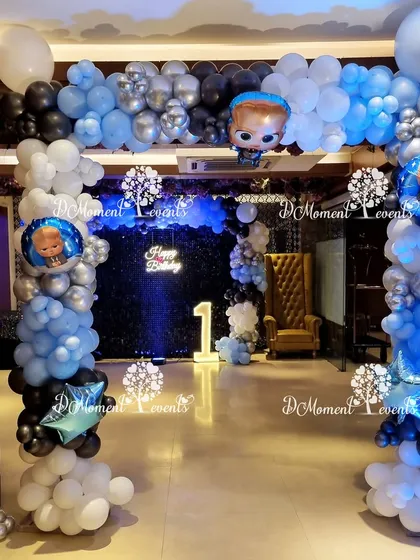 An elegant entrance for a "Boss Baby" party, with a balloon arch in shades of blue, black, and silver leading to a moody, backlit photo area.