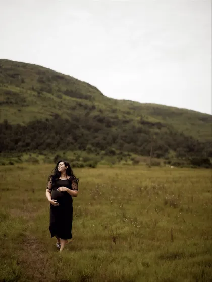 A beautiful wide shot of the mom-to-be walking through a field, cradling her bump. The vast landscape emphasizes the personal and profound journey she is on.