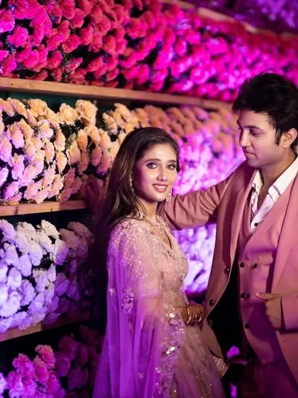 The couple poses against a stunning floral wall, their coordinated pink outfits complementing the decor. This shot is a perfect example of a stylish and modern engagement portrait.