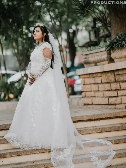 A full-length shot of the bride in her beautiful white wedding gown with a long, elegant train, posing on the steps.