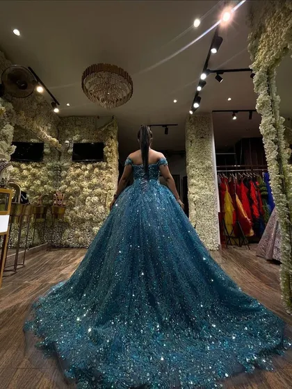 A client trying on a magnificent teal-blue sparkling ball gown. This back view shows the incredible volume and shimmer of the dress against our flower wall.
