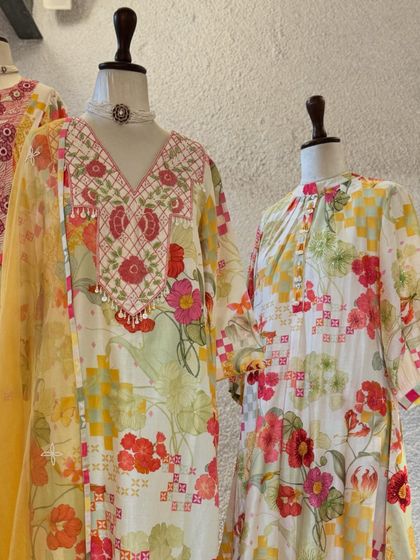 A display of festive floral suits, featuring bright, cheerful prints on white and yellow bases, perfect for daytime events.